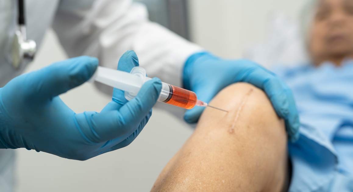 A doctor is giving an injection to a patient in a hospital bed getting Regenerative Joint Repair Treatments NJ and NYC at Victory Medical Institute