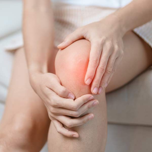 A woman is sitting on a couch holding her knee in pain. Shockwave Therapy