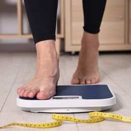 A person is standing on a scale next to a measuring tape checking her progress with medical weight loss