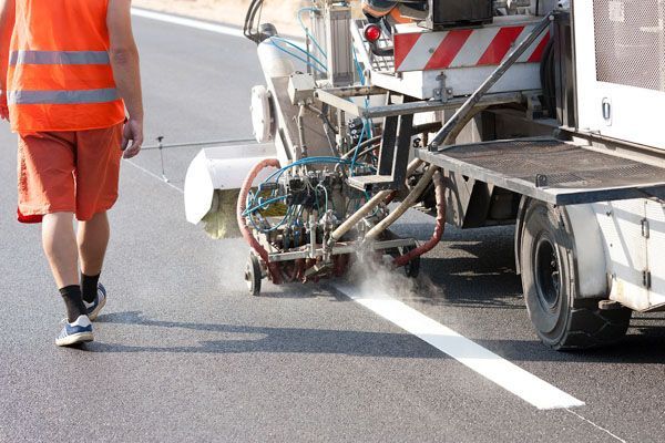 a man is walking past a machine that is painting a line on the road .