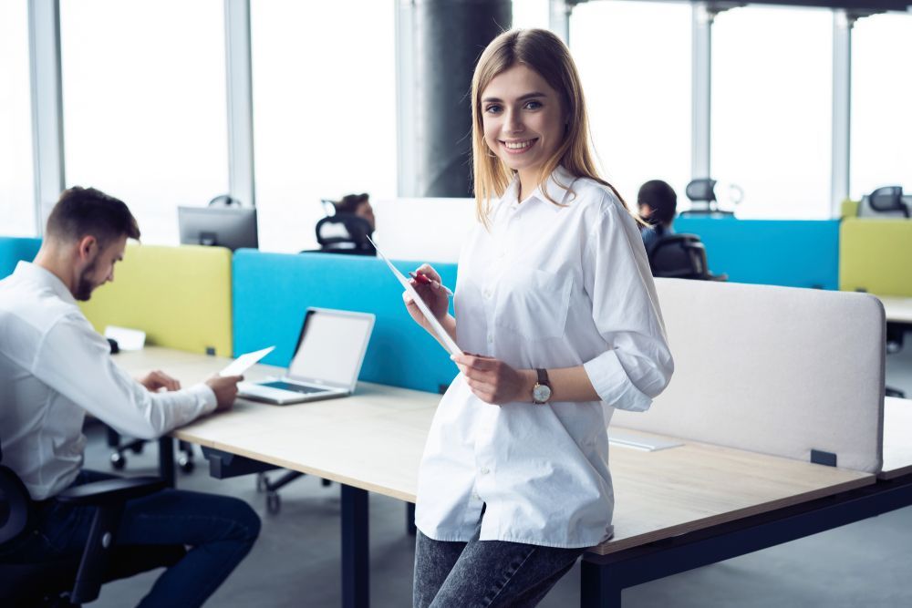 A woman is standing next to a desk in an office holding a tablet with the cost-benefit analysis of the company's PEO