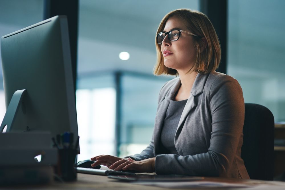 A woman is sitting at a desk in front of a computer researching the pros and cons of a PEO