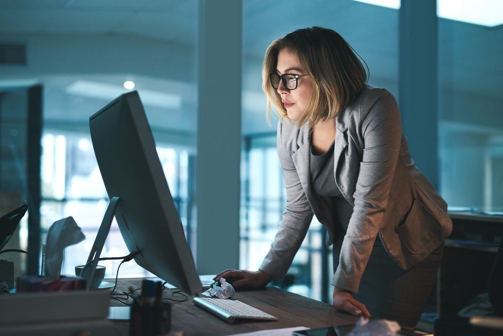 A woman standing in front of a computer reading the pros and cons of PEO for her small business.