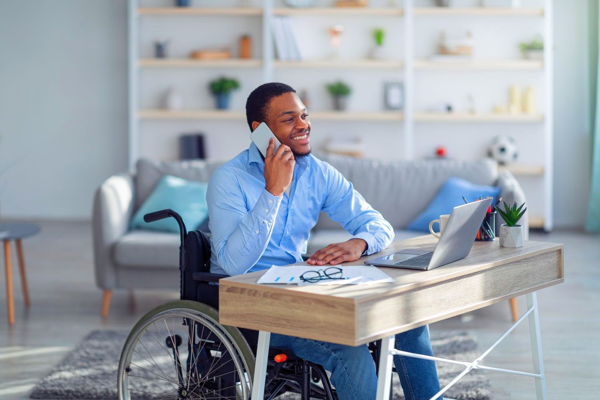 a man in a wheelchair is sitting at a desk talking on a cell phone with a disability insurance broker