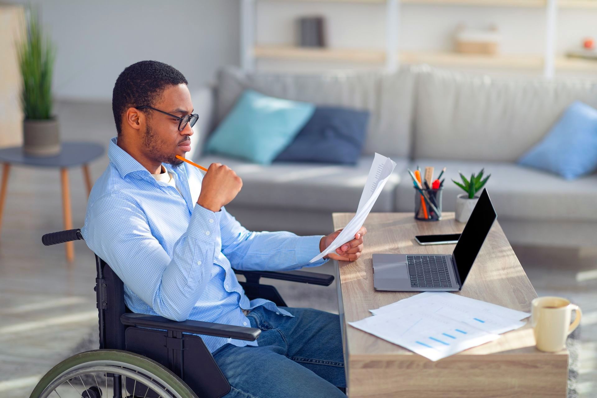 a man in a wheelchair is sitting at a desk looking through insurance documents, his company would benefit from a disability insurance broker