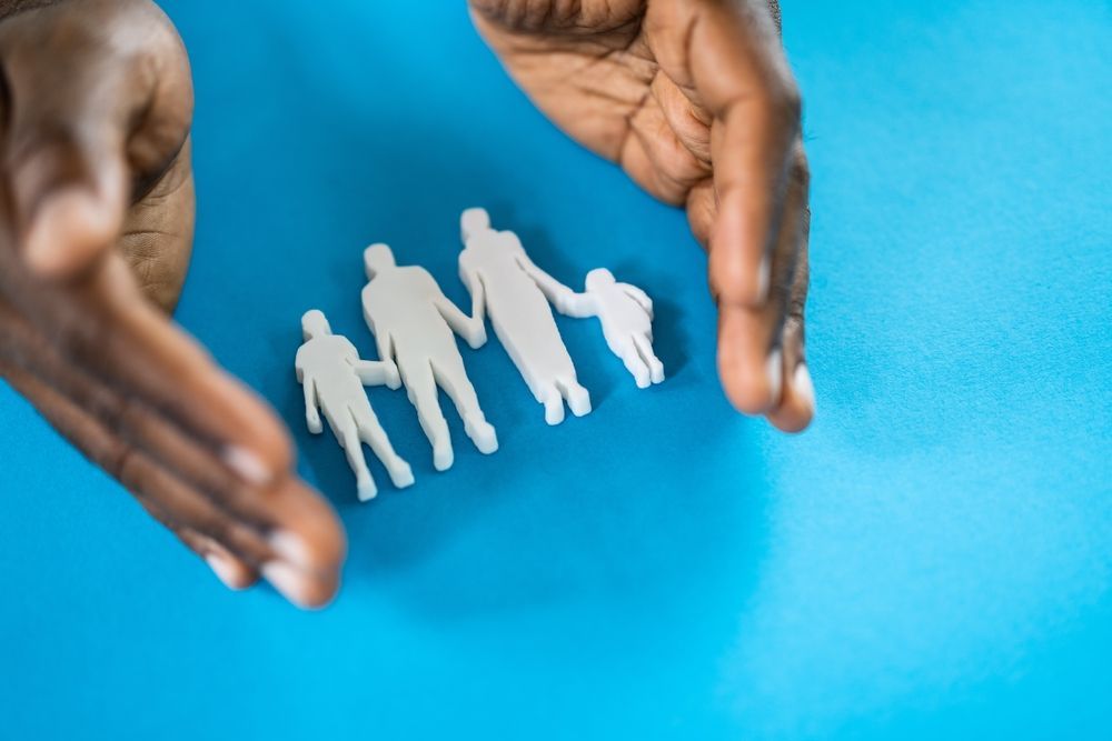 a person is holding a model of a family in their hands representing the benefits of group health insurance