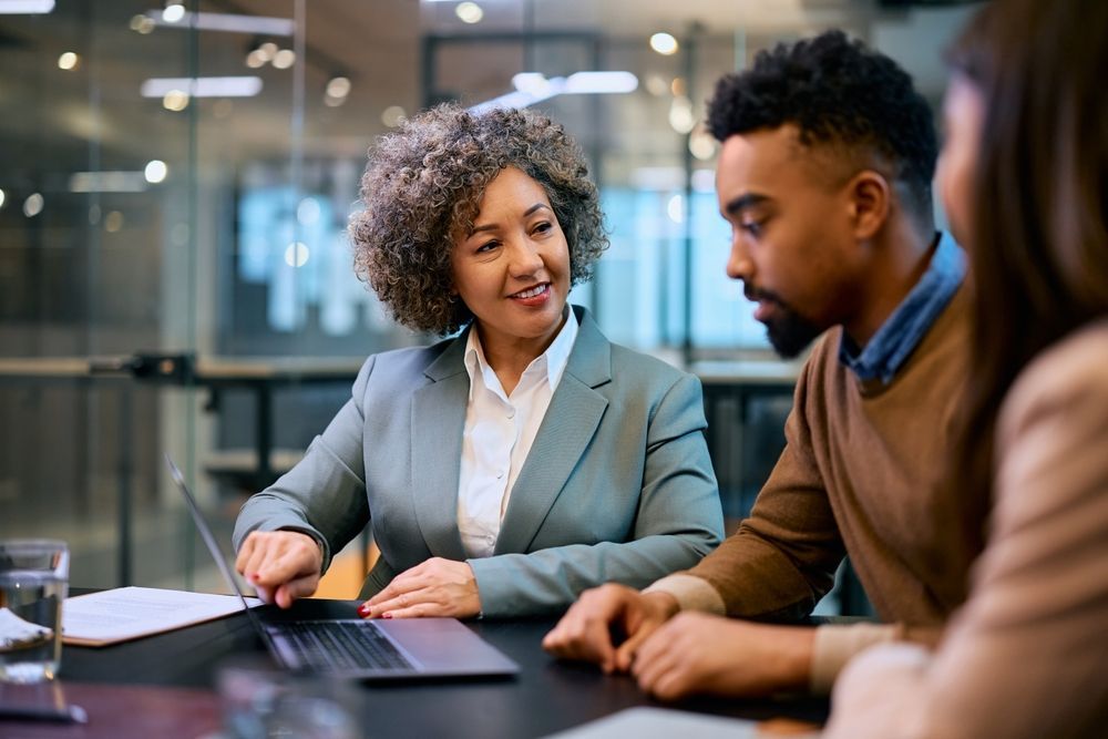 A man and a woman are sitting at a table looking at a laptop.