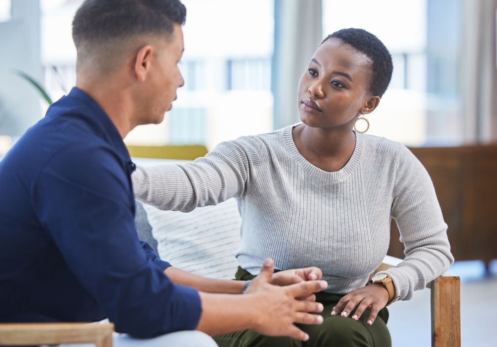 A man and a woman are sitting in chairs talking to each other.