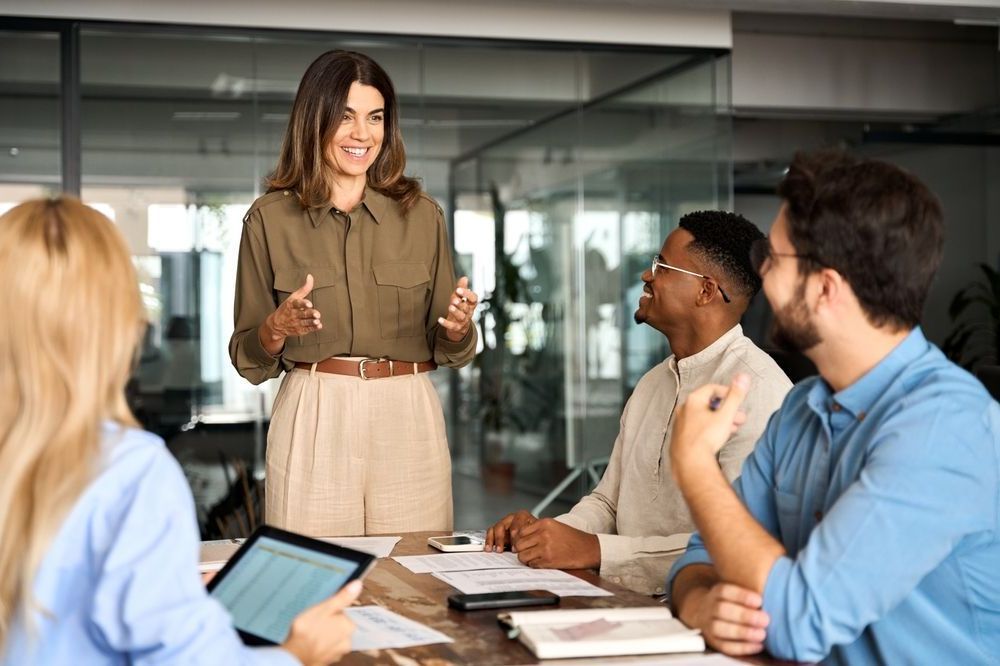 A woman is giving a presentation to a group of people sitting around a table.