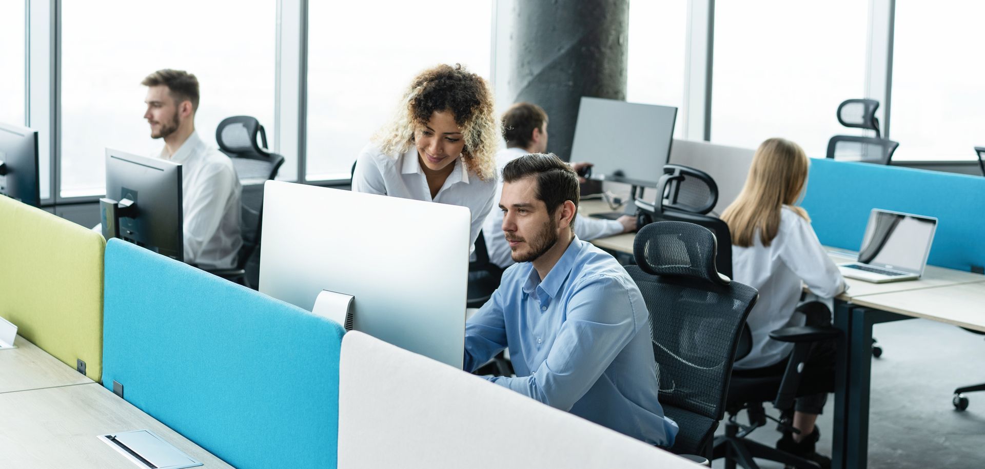 A group of people are sitting at desks in an office working on computers and reviewing their company