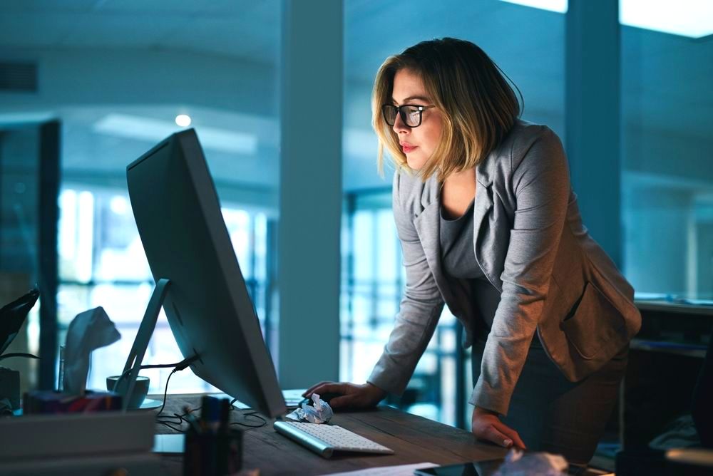 A woman standing in front of a computer reading the pros and cons of PEO for her small business.