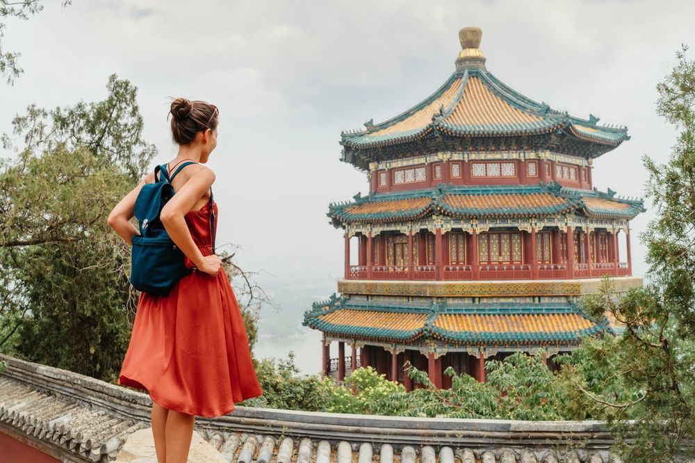 A woman in a red dress is standing on a roof looking at a pagoda.