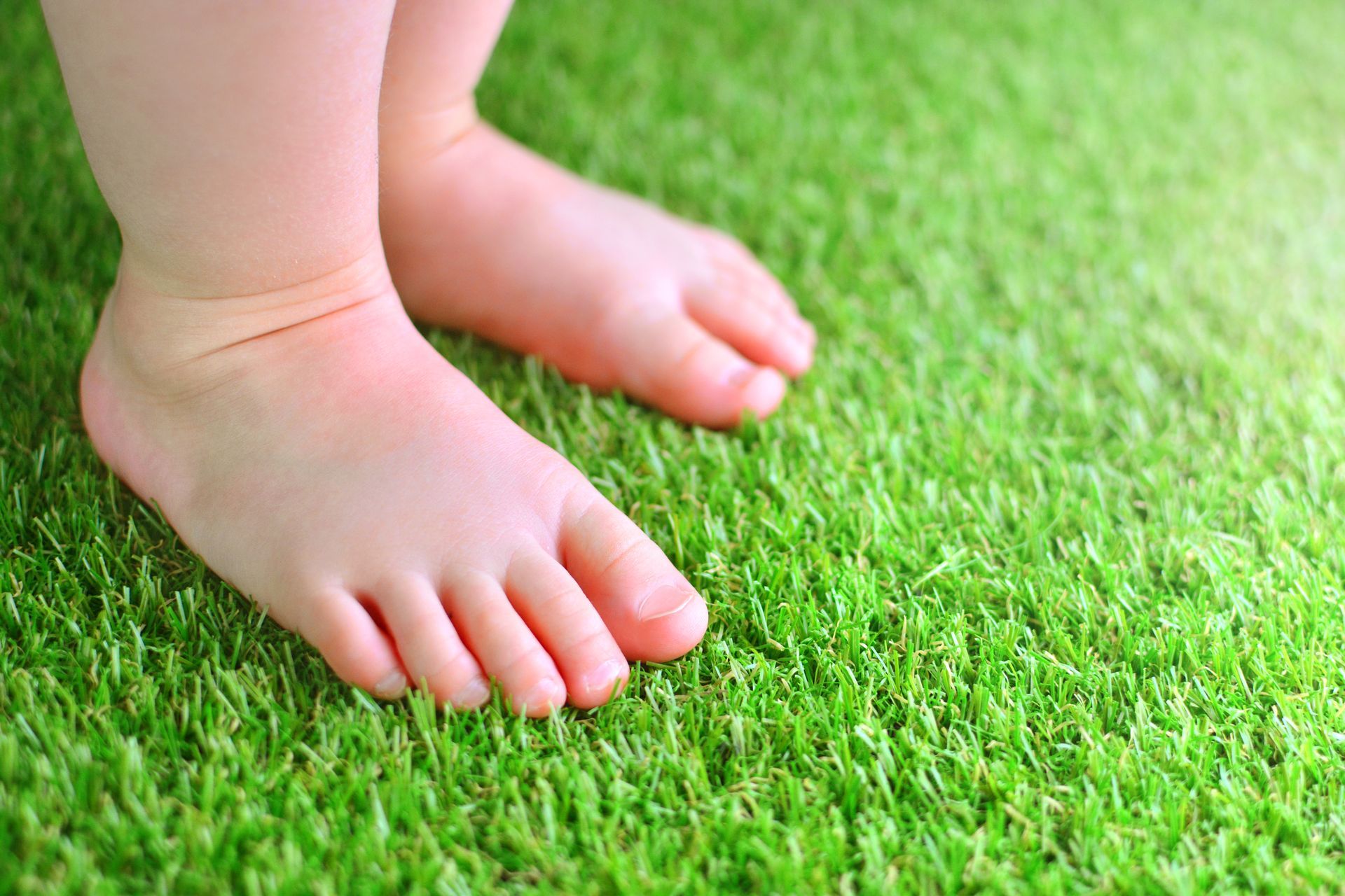 Benefits of installing turf: Feet of a baby on a green artificial turf