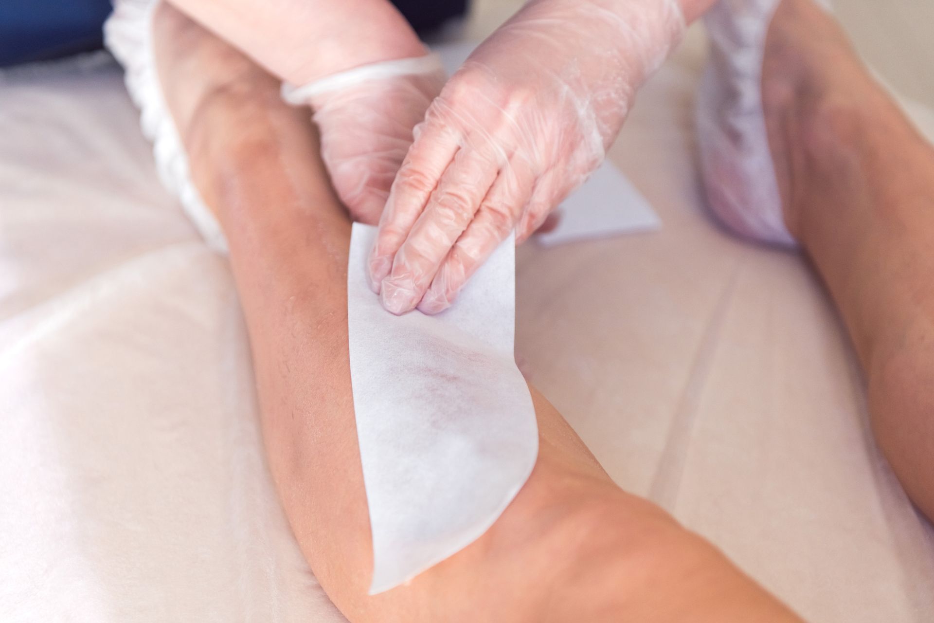 Hands waxing a person’s leg with a white wax strip in a spa setting