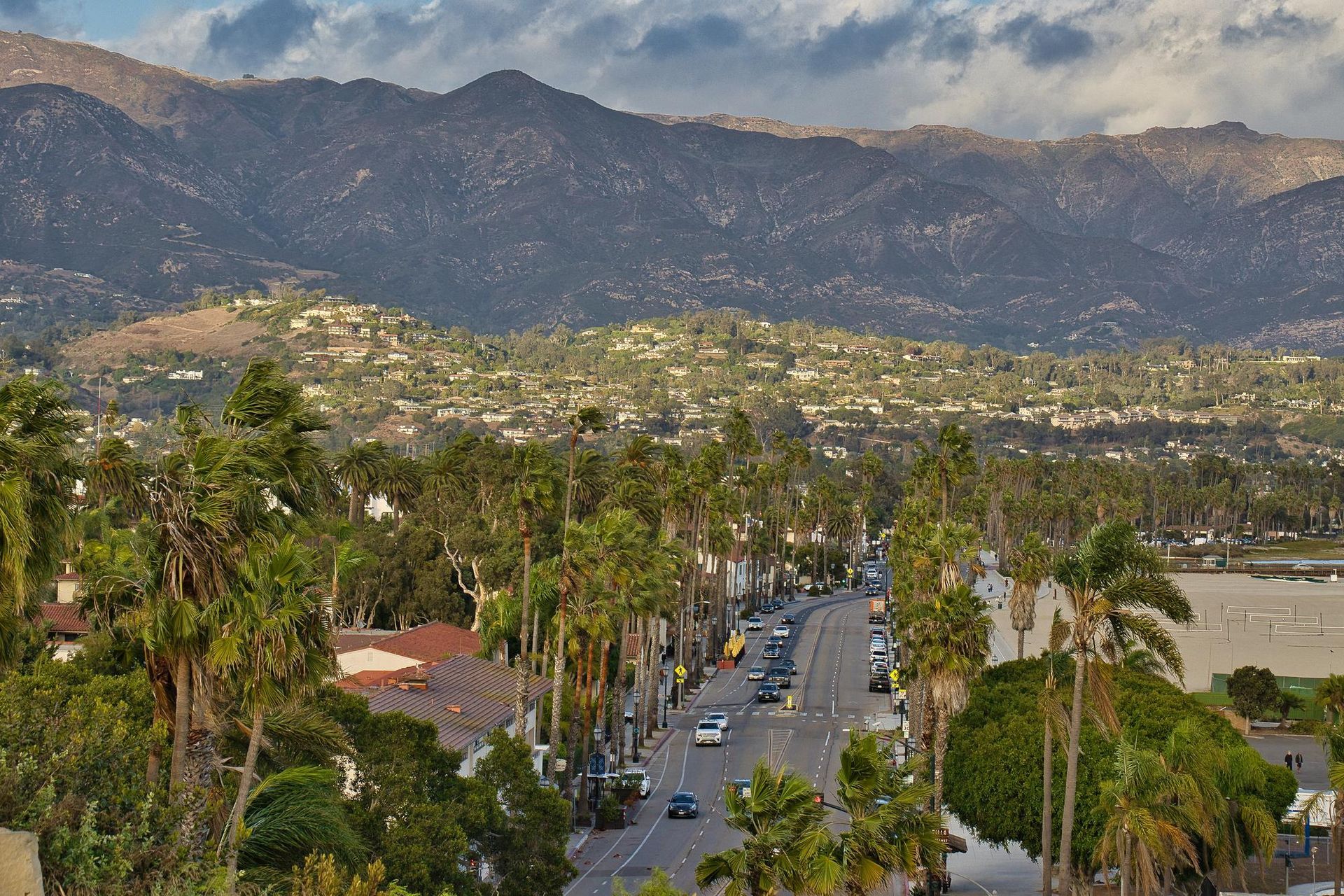 Street lined with palm trees, cars, and buildings, with mountains in the background, Santa Barbara, California.
