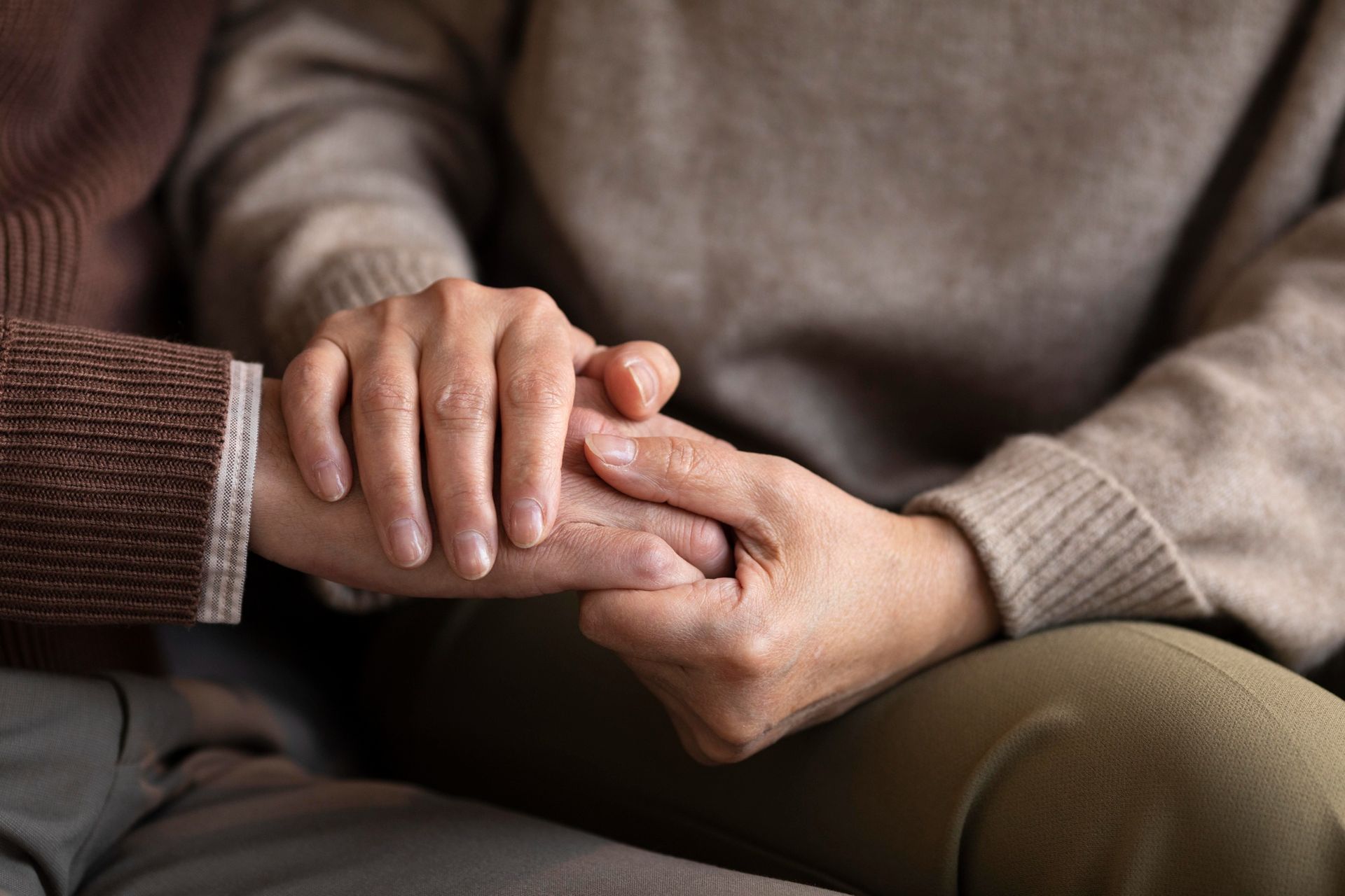 Two people holding hands, offering comfort. Neutral tones, close-up view.