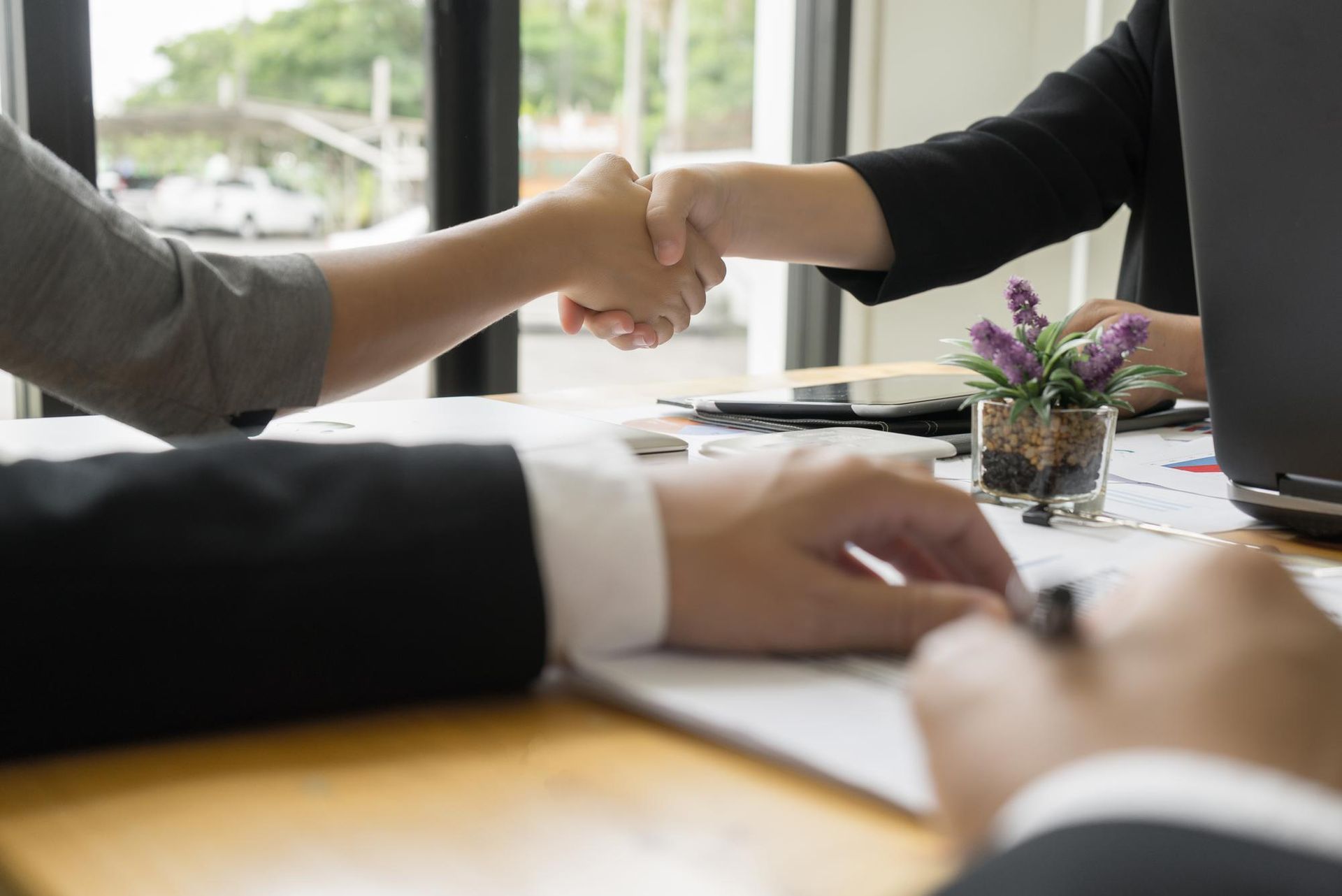 Two people shaking hands over a table in an office setting.