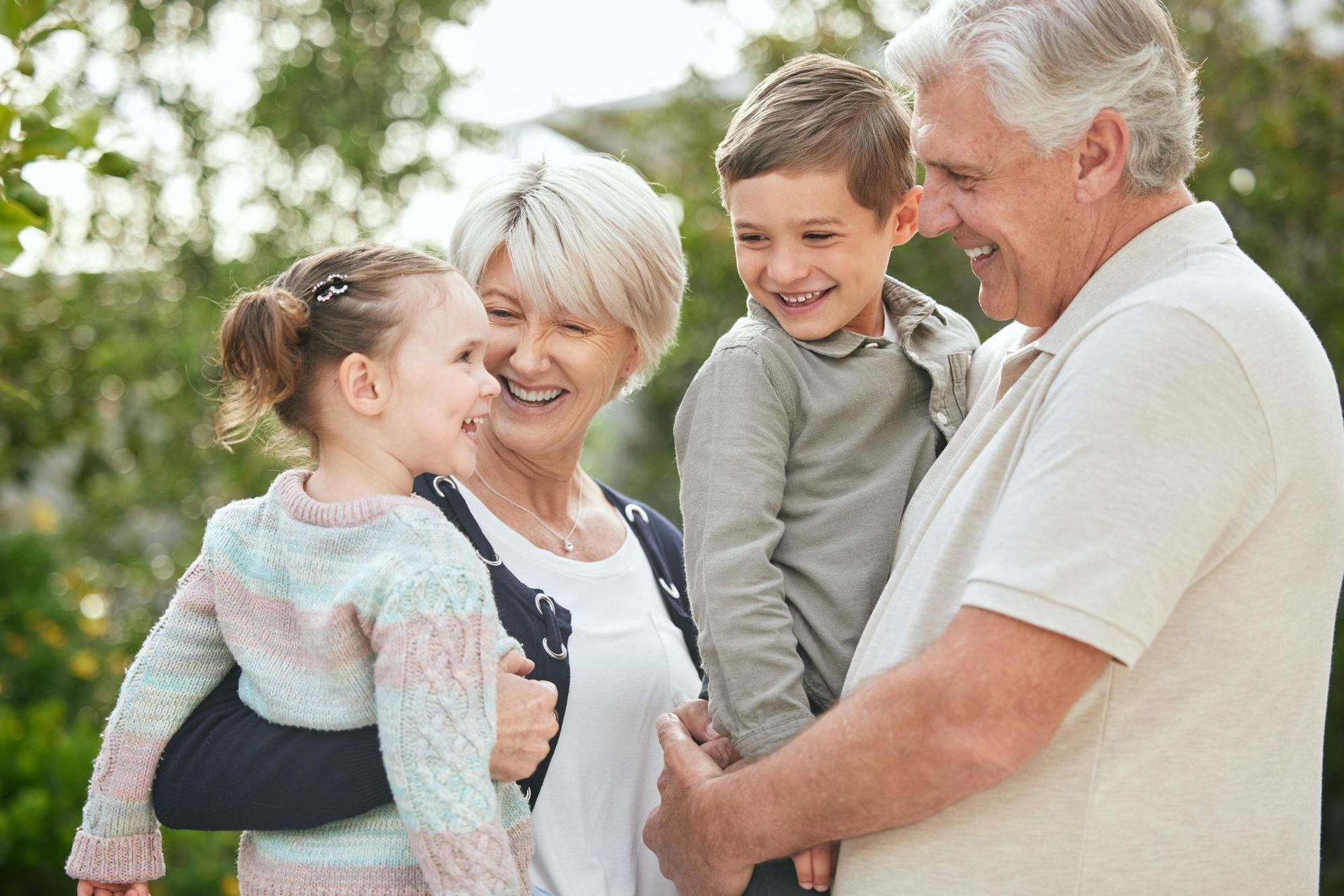 Grandparents smiling with young grandchildren outdoors.