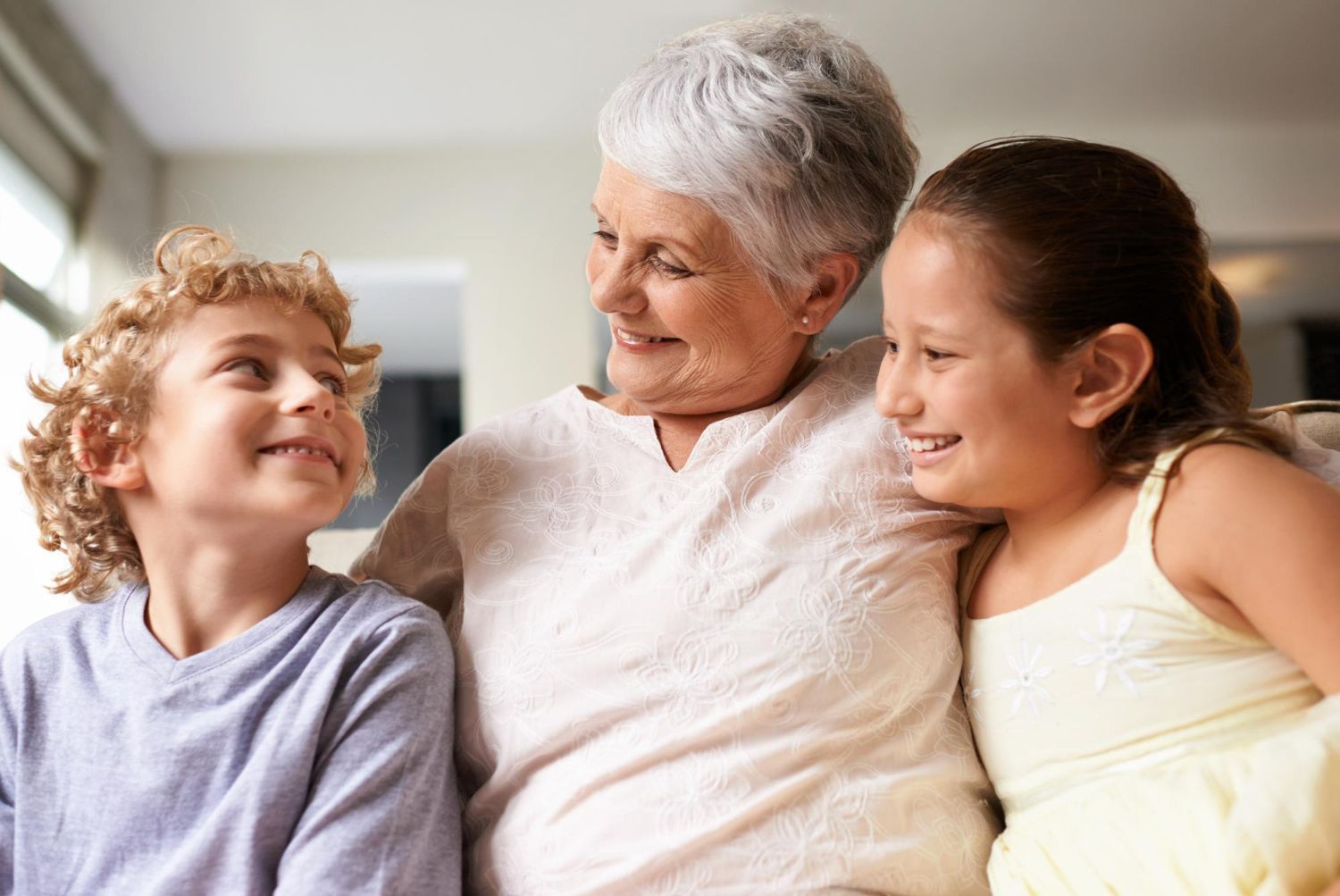 Grandmother smiling at two grandchildren, boy and girl, indoors.