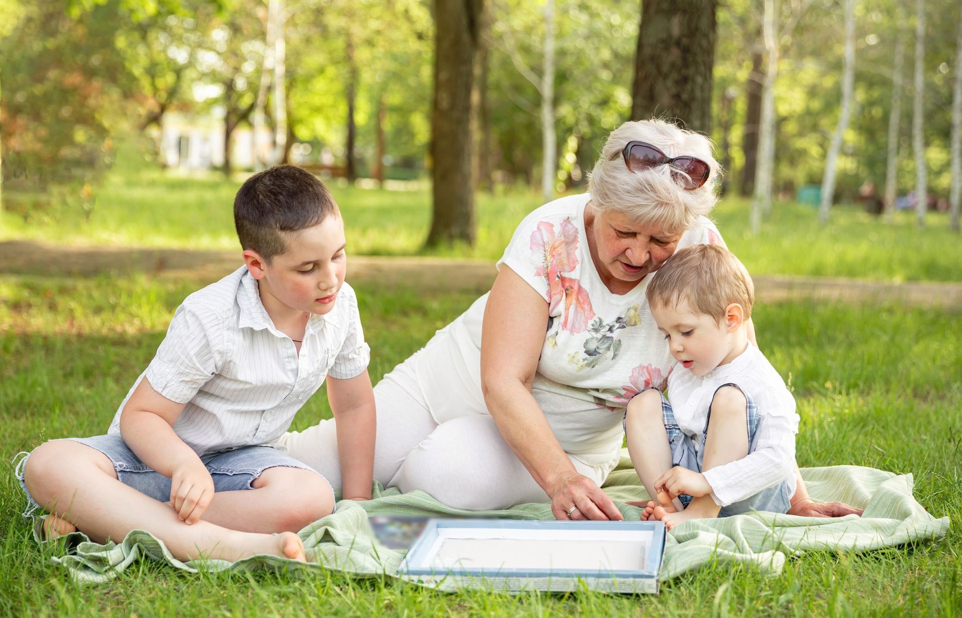 Grandmother reading with two grandsons on a blanket in a park.