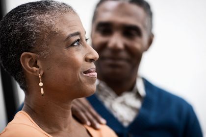 Smiling Black woman with man's hand on her shoulder, possibly couple, looking off camera.