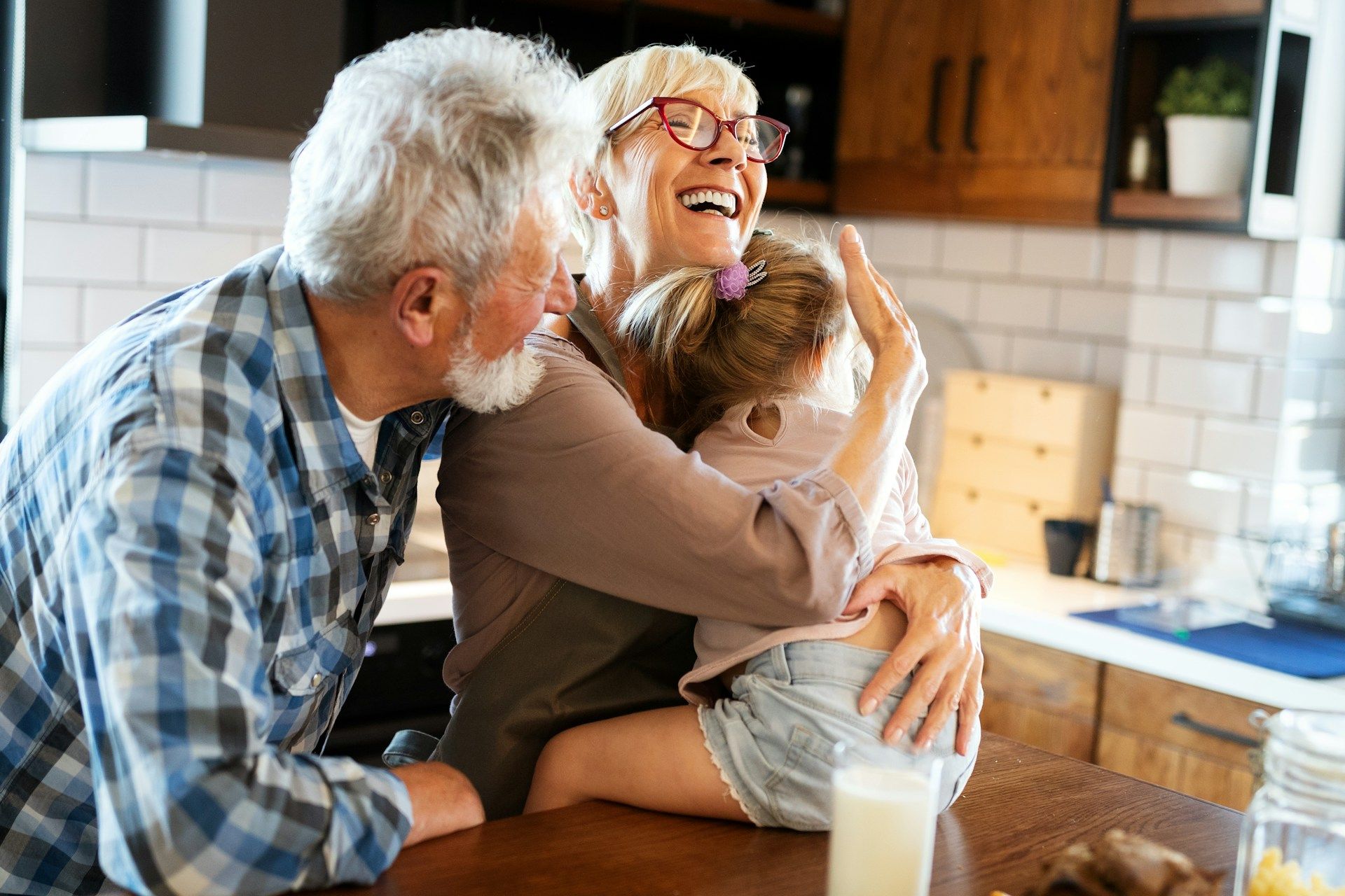 Smiling older couple looking at a phone together, beside an open laptop and a coffee cup.