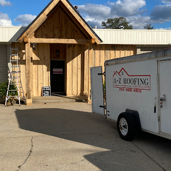 A white a-z roofing trailer is parked in front of a wooden building