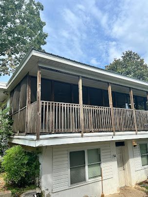 A white house with a screened in porch and a wooden railing.