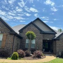 A large brick house with a gray roof and a tree in front of it.