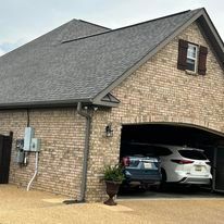 A car is parked in a garage next to a brick house.