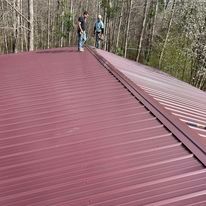 Two men are standing on top of a red metal roof.
