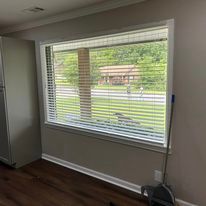 A room with a large window with blinds and a broom.