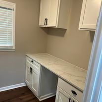 A laundry room with white cabinets , a desk , and a window.