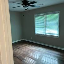 A bedroom with hardwood floors , a ceiling fan , and two windows.
