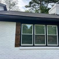 A white brick house with three windows and a black roof.