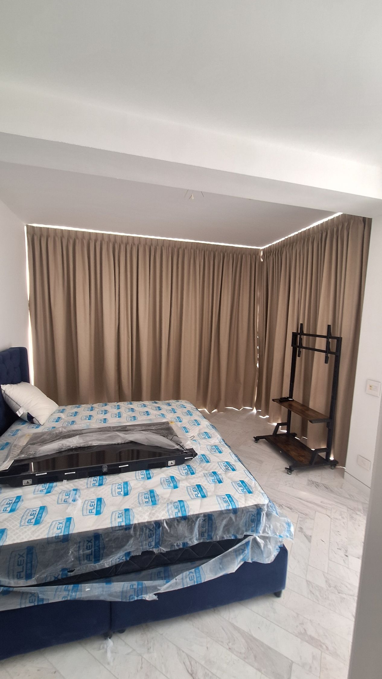 Dormitorio con cama, cortinas y mueble para TV; paredes blancas.