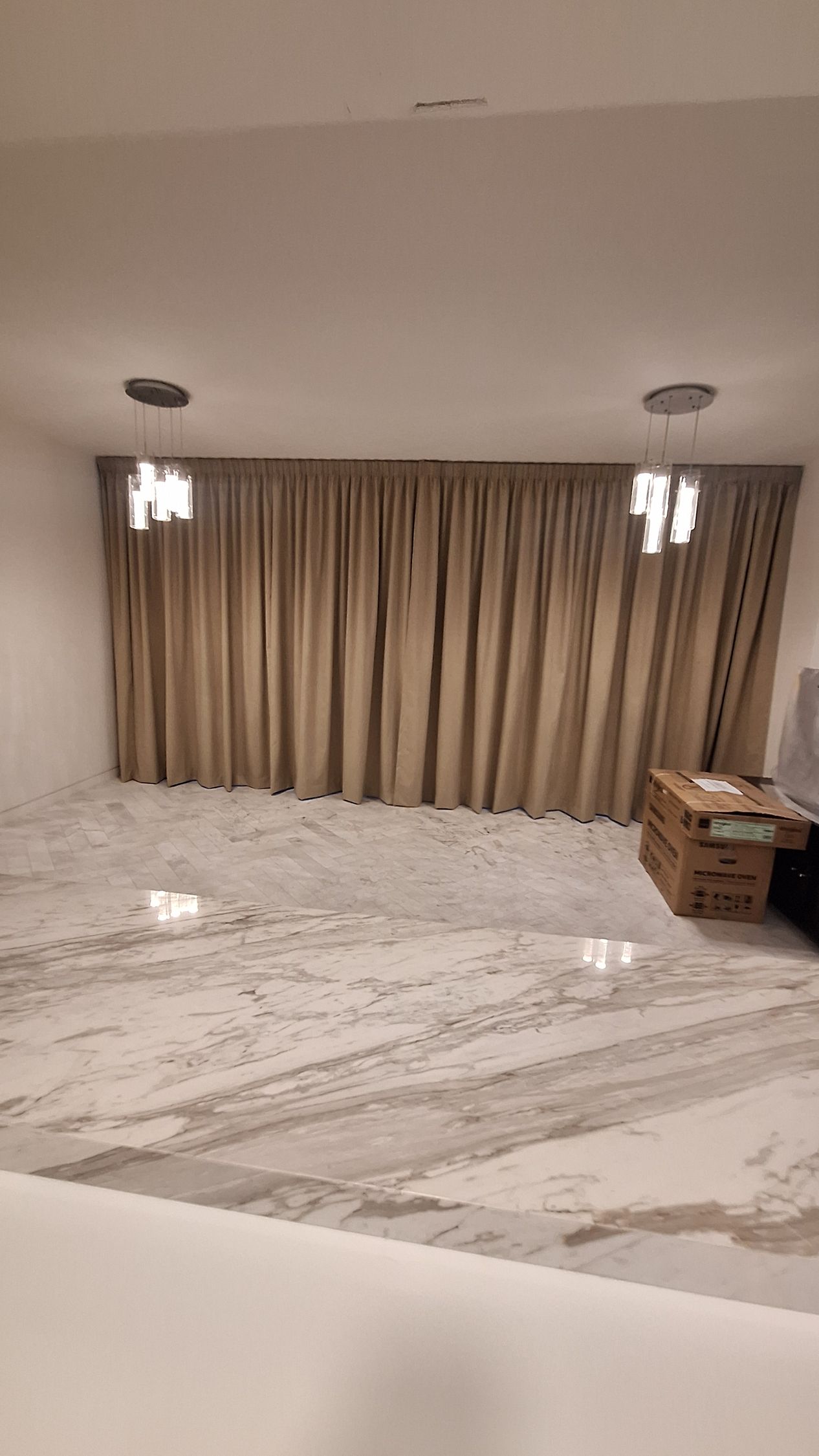 Cortinas beige, dos lámparas de araña y suelo de mármol en una habitación moderna.