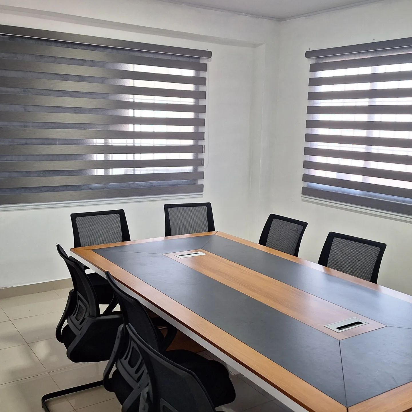 Sala de reuniones con mesa grande, seis sillas y dos ventanas con persianas cerradas.