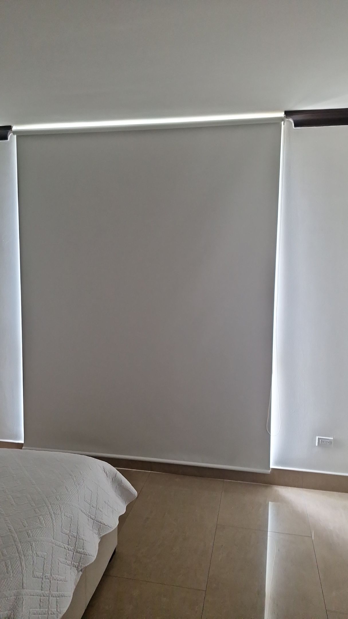 Dormitorio con persianas enrollables grises y paredes blancas.