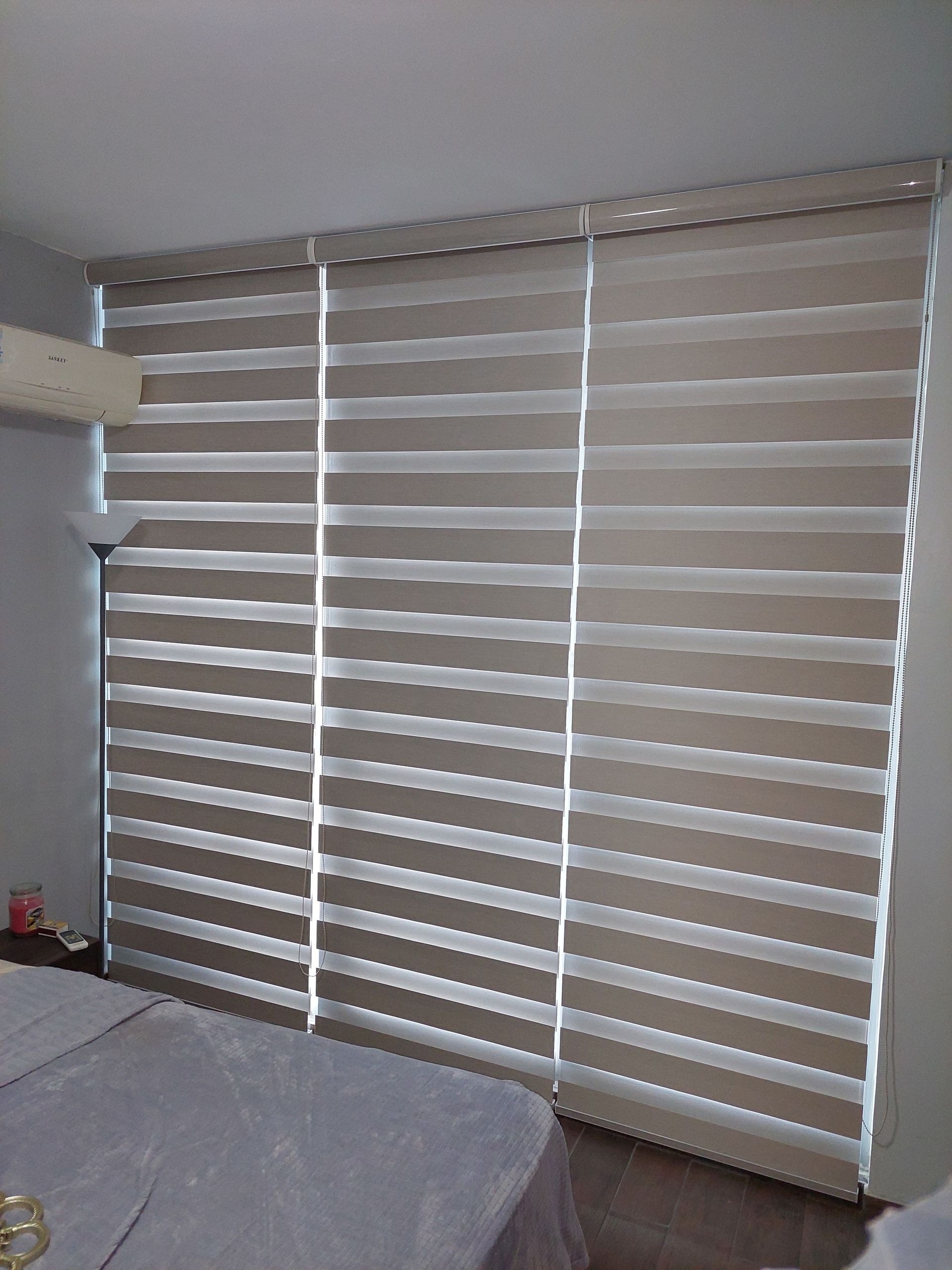 Persianas de rayas beige y blancas que cubren una ventana en un dormitorio.