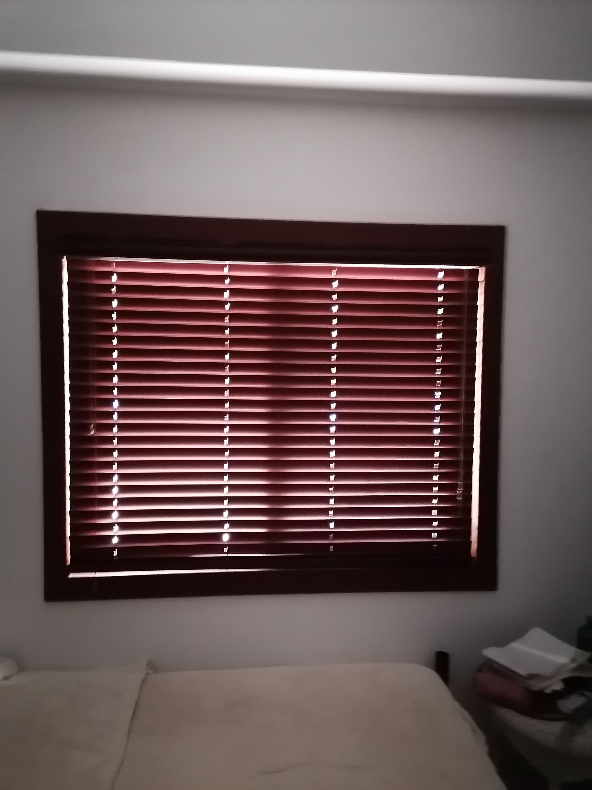 Ventana con persianas cerradas de color marrón rojizo, dentro de un marco de madera oscura, sobre una pared blanca.