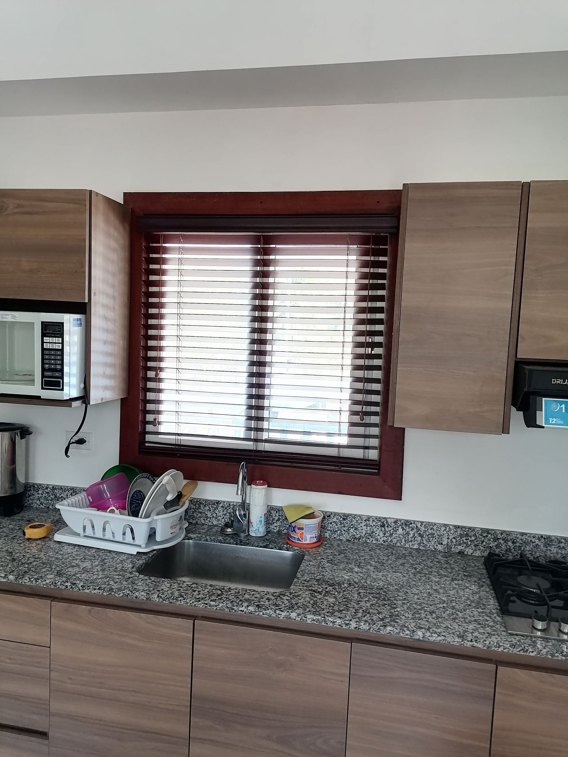 Cocina con gabinetes de madera, ventana con persianas, cubierta de granito y fregadero.
