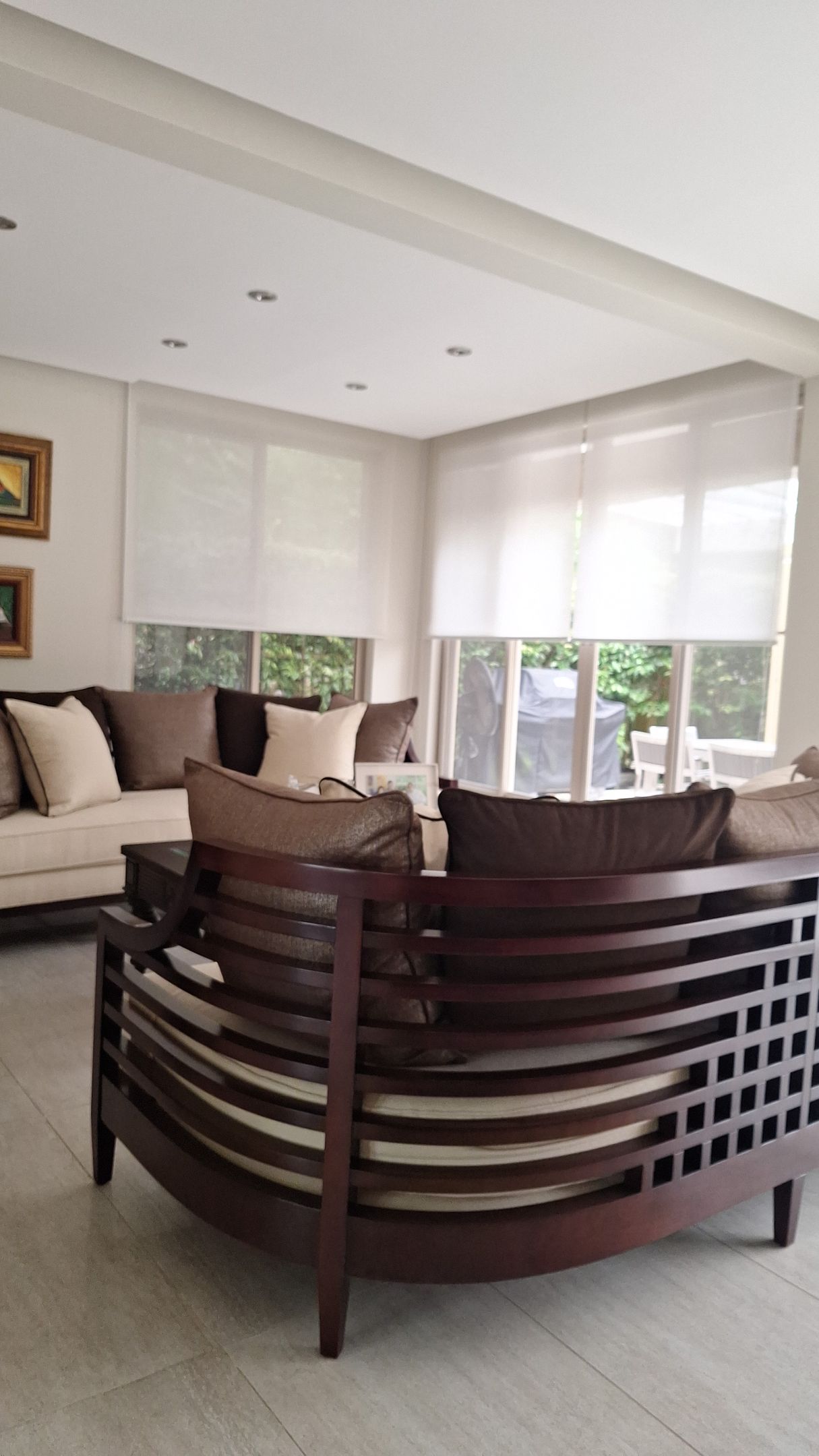 Sala de estar con sofá de madera curvo, paredes neutrales y cortinas; luminosa y aireada.