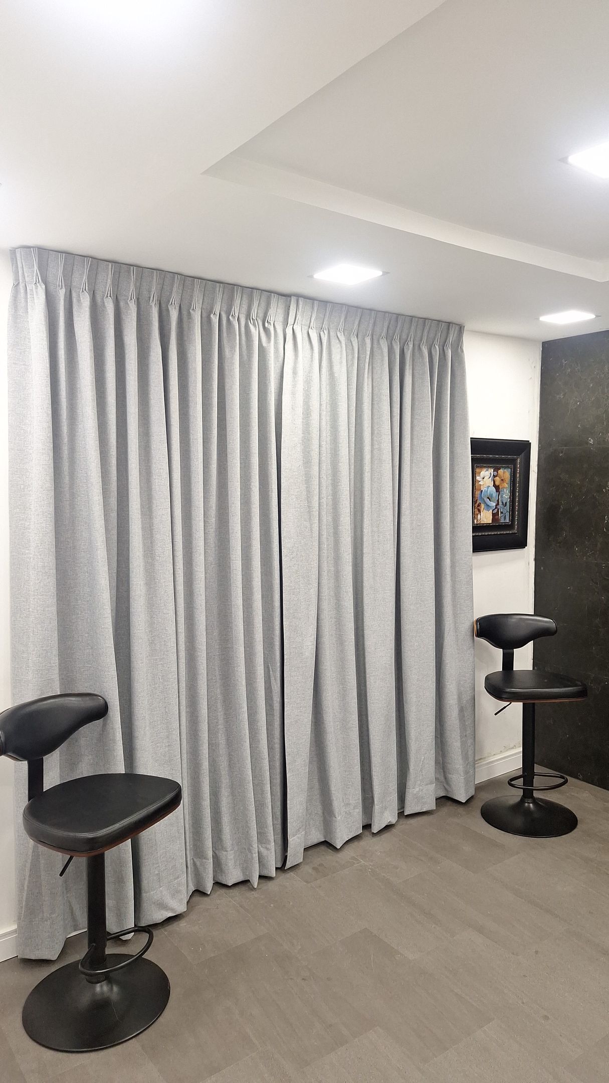 Dos taburetes de bar negros frente a cortinas gris claro, habitación con pared oscura y pintura.