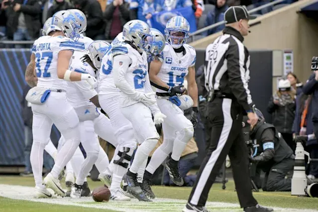 A group of football players are running on the field while a referee watches.