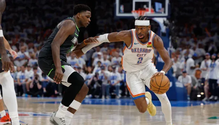 A basketball player is dribbling the ball while another player tries to stop him.