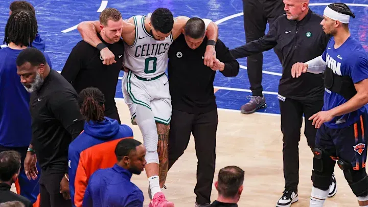 A basketball player is being helped off the court during a game.