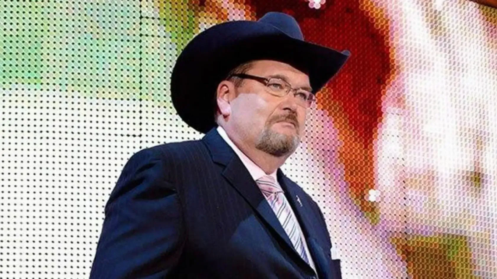 A man in a suit and cowboy hat is standing in front of a screen.