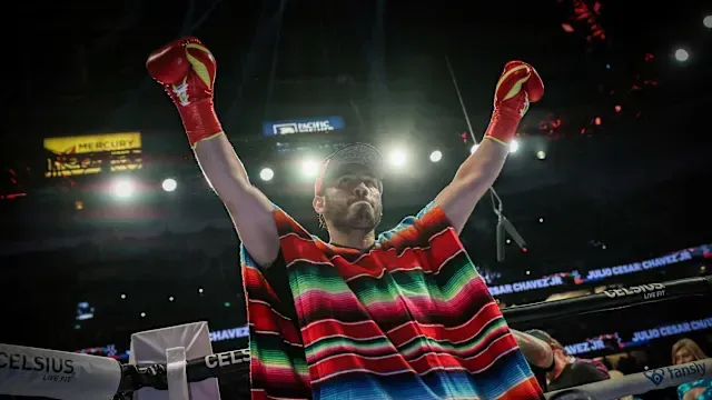 A man wearing a mexican poncho and boxing gloves is standing in a boxing ring.