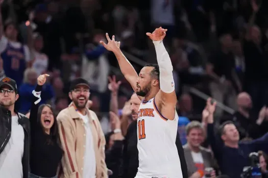 A basketball player is standing in front of a crowd with his arms in the air.